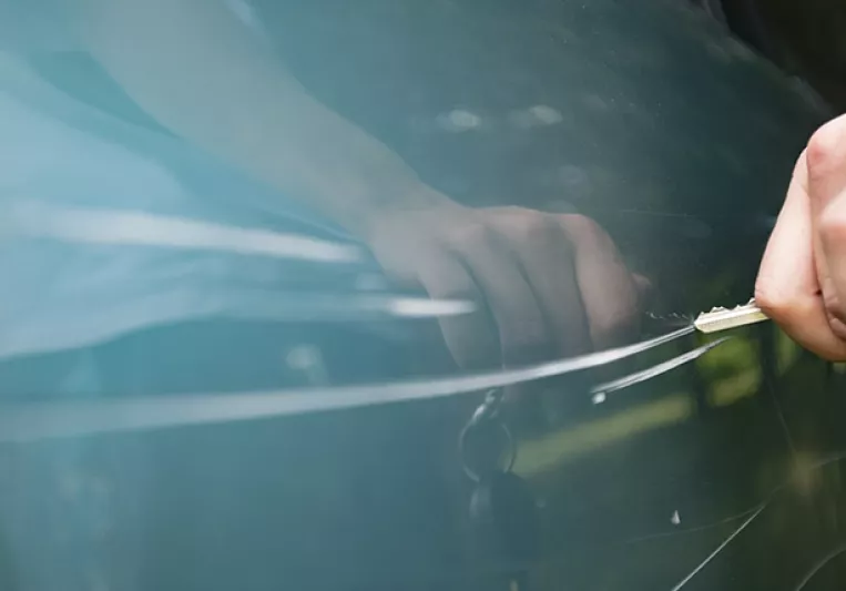 Una mano rayando la puerta de un coche