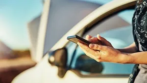 Mano con móvil fuera de la ventanilla de un coche